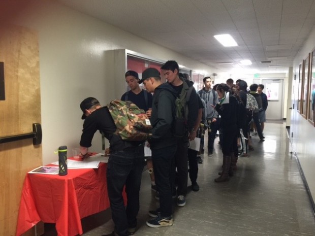 Students in hallway signing-up at table.